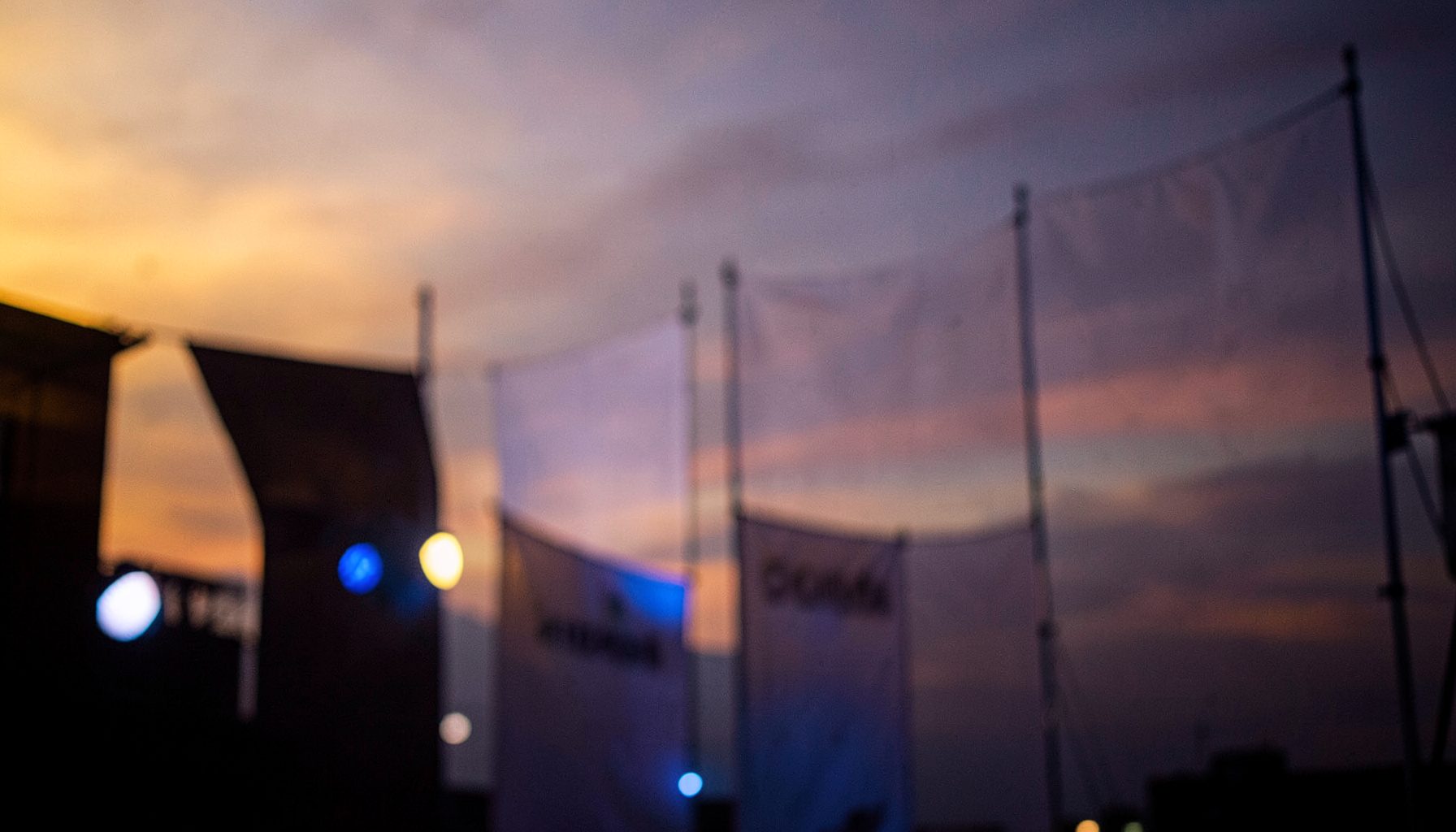 A close-up of stage-lit studio banners against a warm dusk sky, golden and indigo hues blending at the horizon